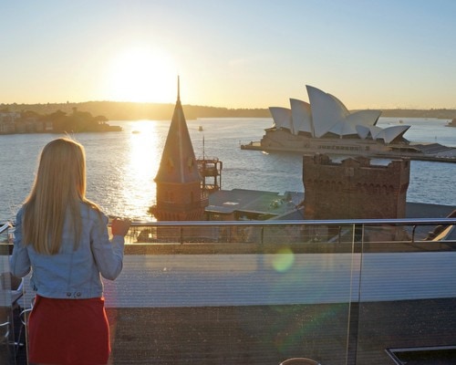 Bright woman enjoying scenic view of Sydney Opera House and harbor during sunset, travel relaxation concept.