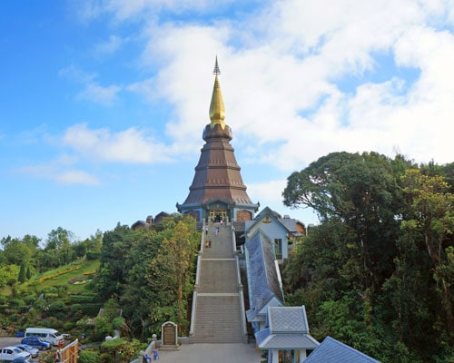 Colorful Buddhist temple on hilltop with blue sky and lush greenery in background.