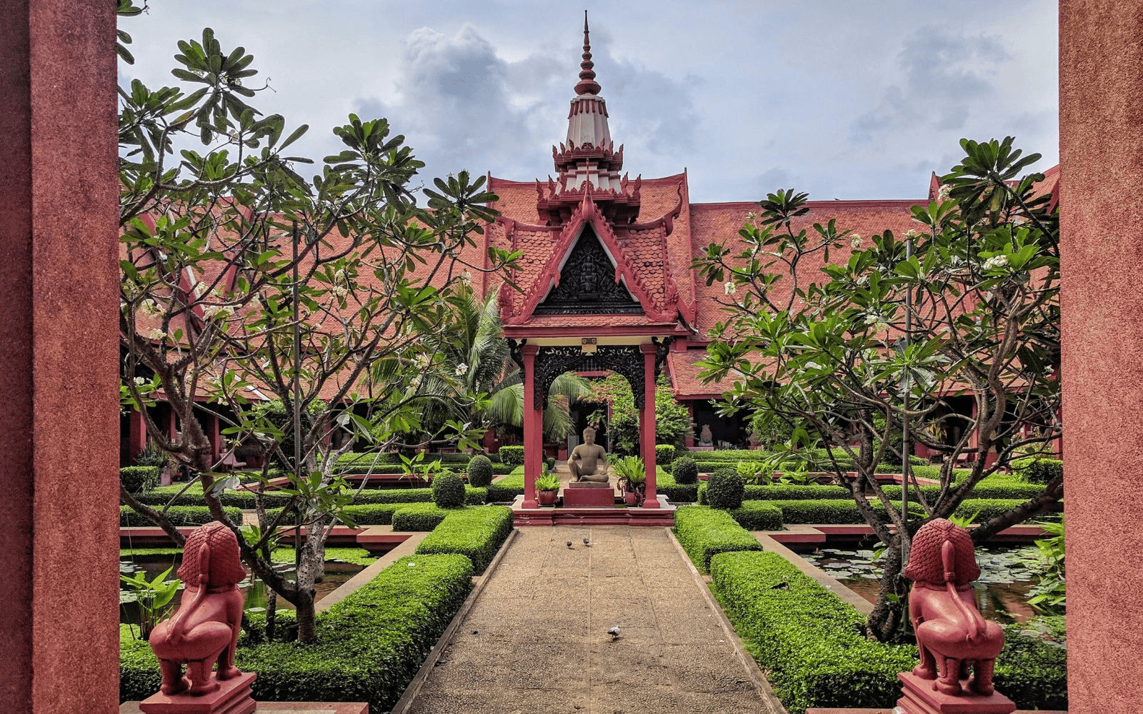 Red sandstone pagoda with Buddha statue and lions in a green garden in Phnom Penh