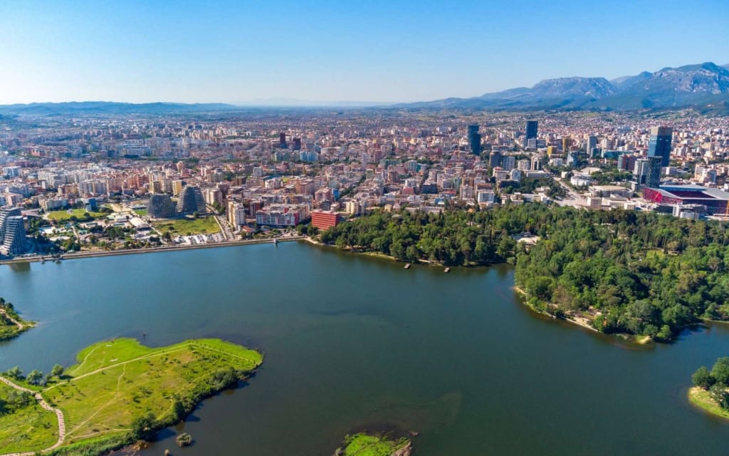 Aerial view of lake in Grand Park, one of the best places to stay in Tirana, cityscape in the background with mountains and a blue sky