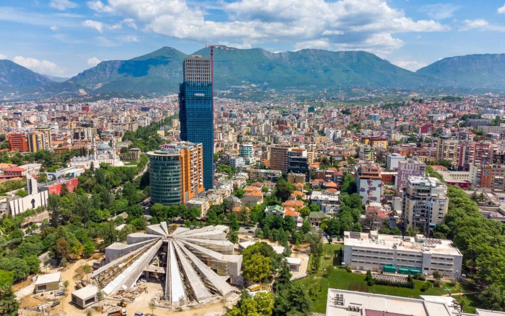 Aerial view of the Pyramid of Tirana and the city against a background of mountains and cloudy sky