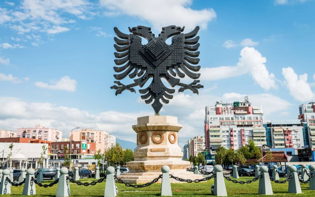 Large statue in city center Tiraana with apartments in the background and blue sky with clouds