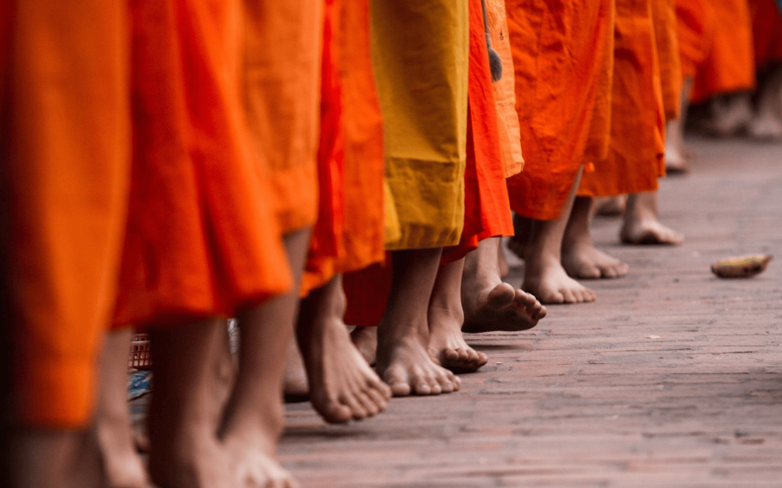 The feet of priests in orange robes practicing a Theravada Buddhism procession in Laos