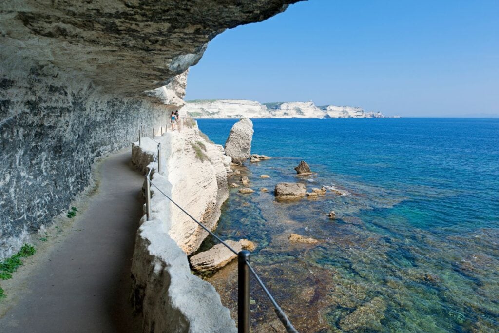 pathway along giant rocks with blue ocean waters on the side