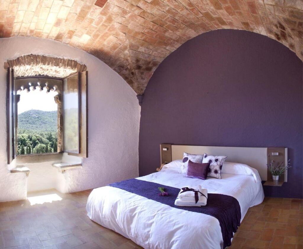 spacious purple room with a cozy bed and nature view from the window