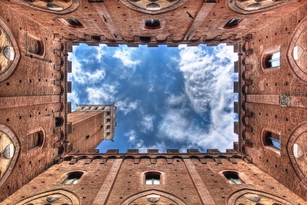 Architectural photo of the interior courtyard of Palazzo Publico Siena against blue sky with clouds