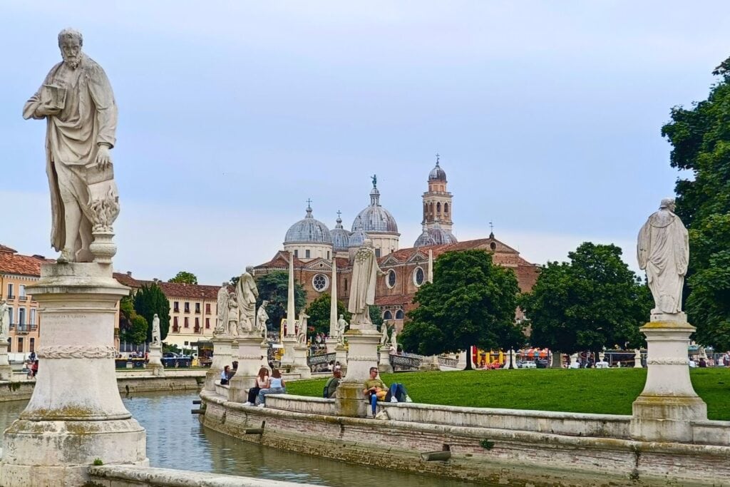 Statues of famous historic figure on canal in Padua with basilica domes in background