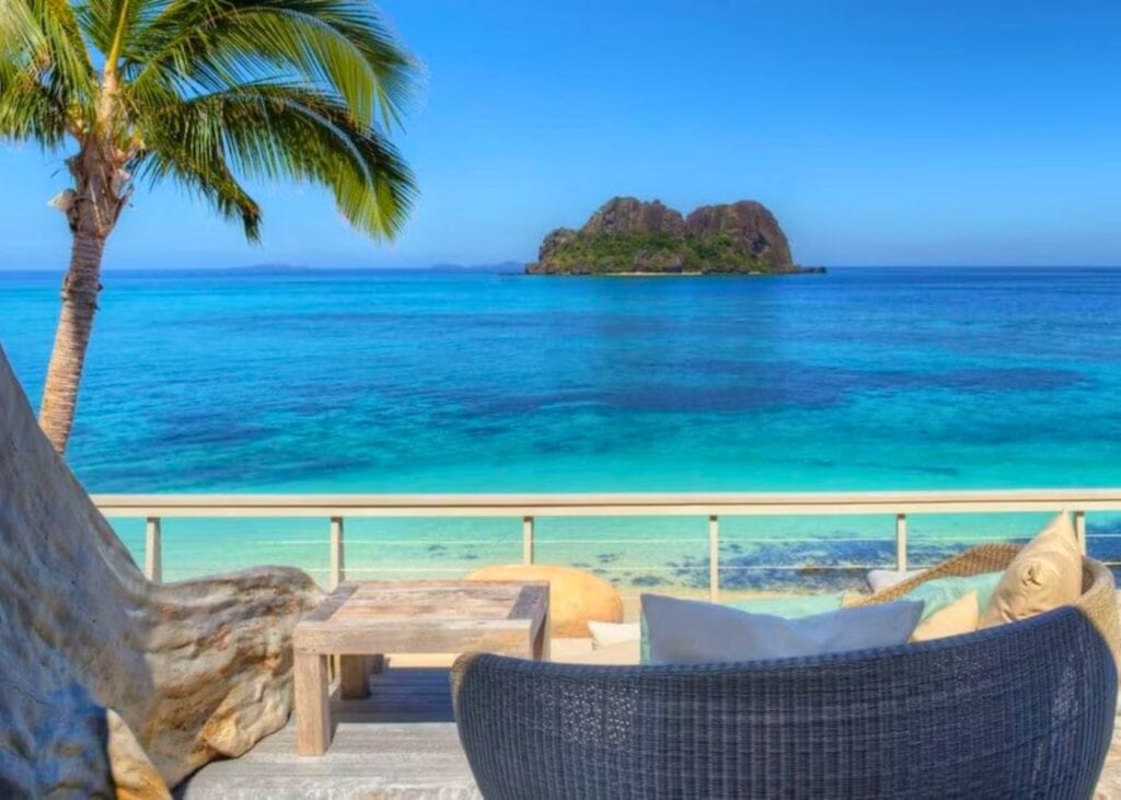 Beachfront villa with lounger and view of rocky island, blue waters, and palm trees at one of the 5-star resorts in Fiji