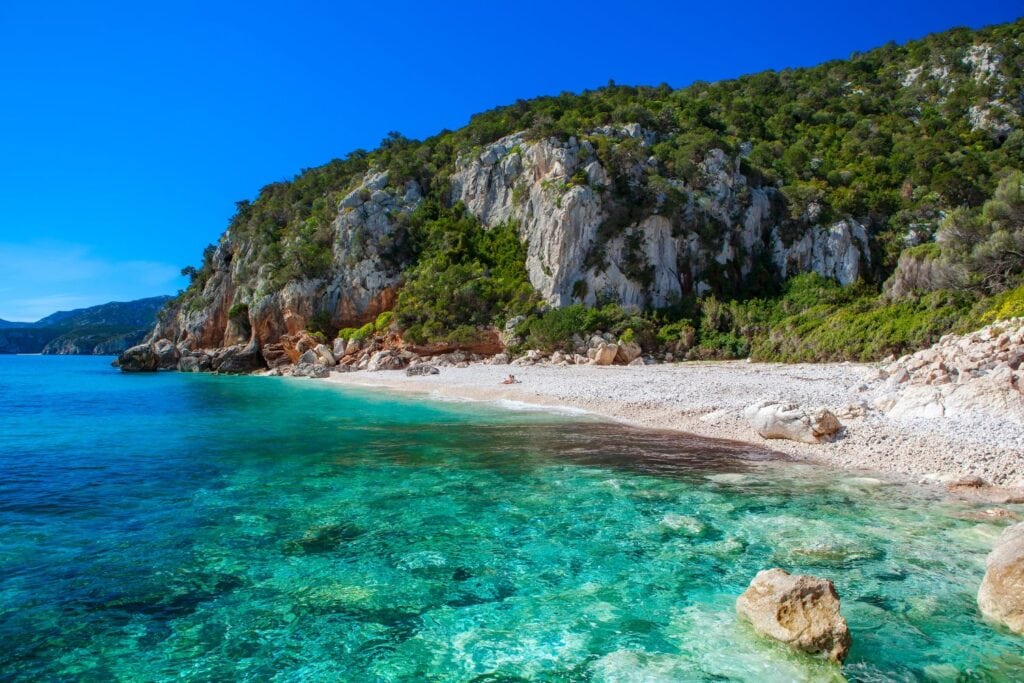 crystal clear waters and beautiful rock formations along the beach with greenery view at Cala Fuili Sardina