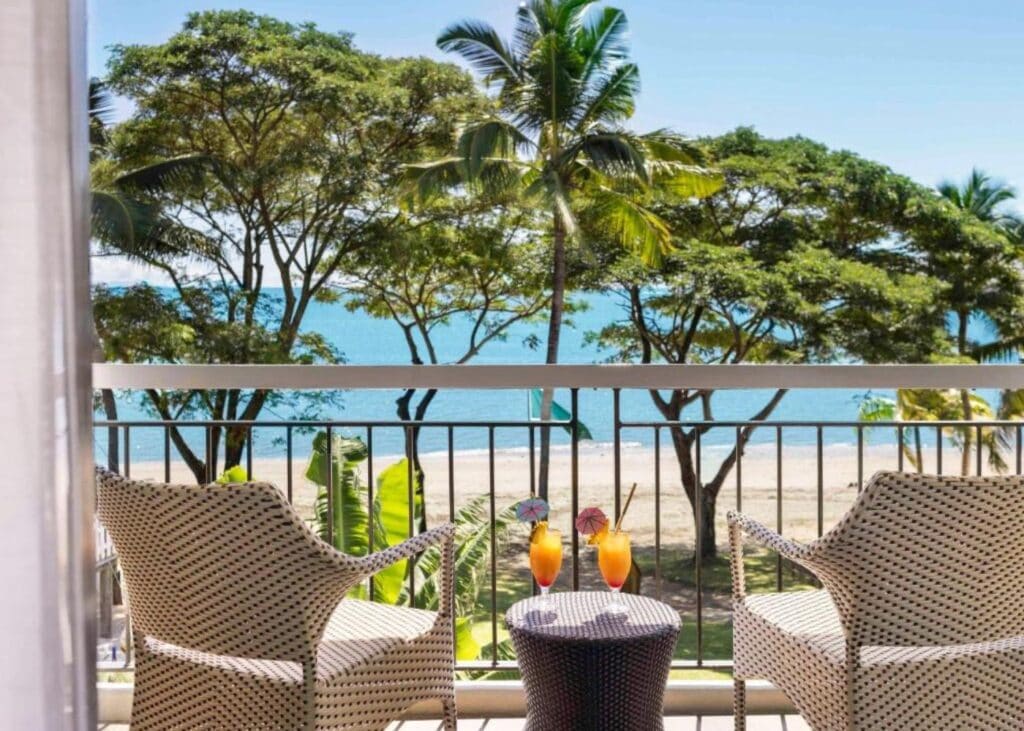 Lounge chairs on a private balcony with orange umbrella cocktails on a white sand beach with tropical gardens
