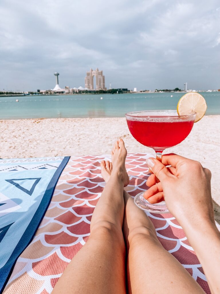 Relaxing beach scene with a cocktail, city skyline, and water views for travel inspiration.