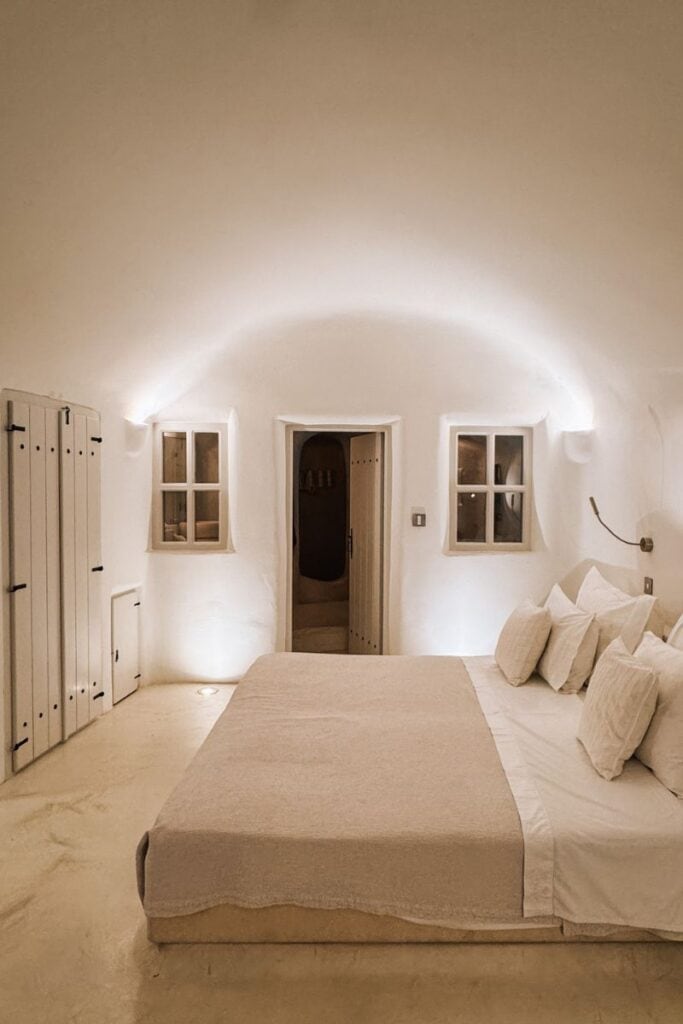 Charming Santorini bedroom with white walls, soft lighting, and minimalist decor, perfect for a romantic getaway in Greece.