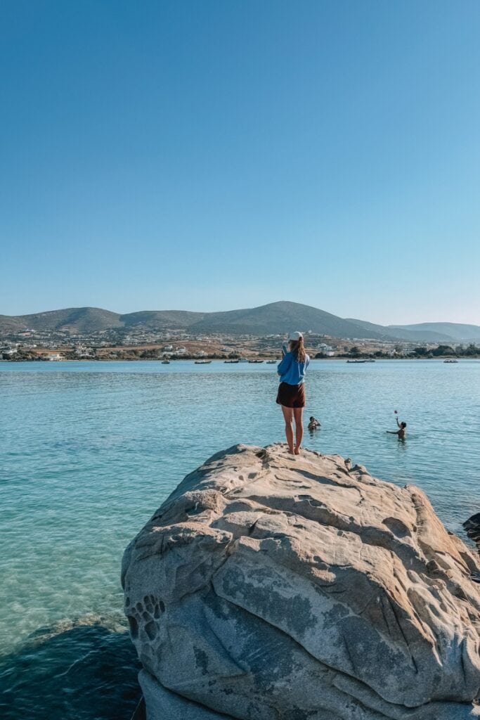Woman standing on a large rock by the sea in Greece, enjoying the view.