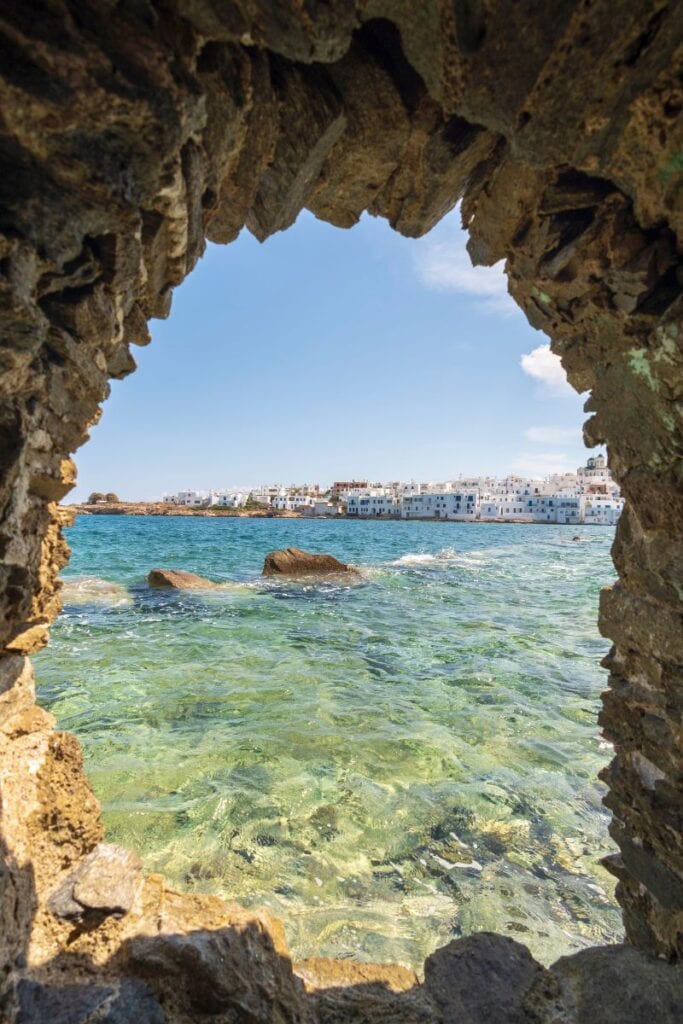 Calm ocean view through a natural rock arch with clear turquoise water and a coastal town in the bac.