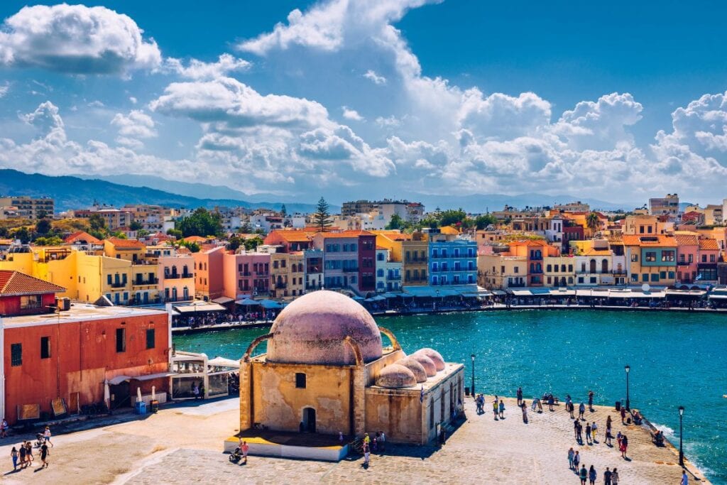Colorful seaside town with historic buildings and a waterfront view under a partly cloudy sky.