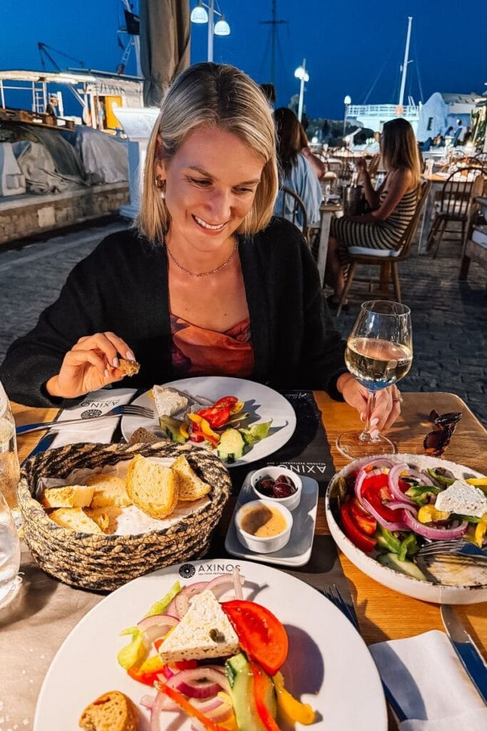 A woman enjoying a seaside dinner with fresh seafood and wine at sunset.