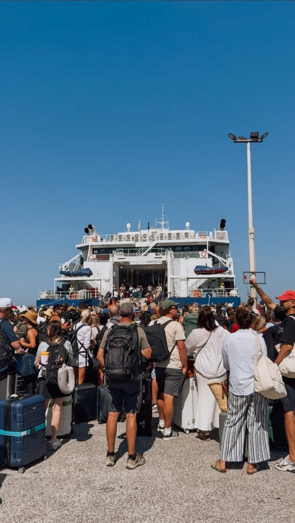 Crowd of travelers boarding a ferry at a busy port under a clear blue sky.